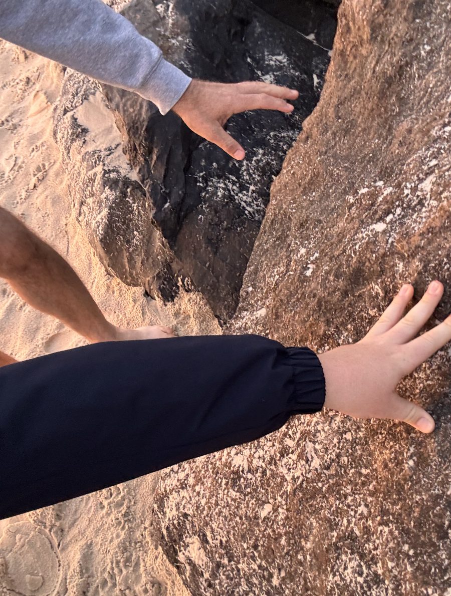 A father's hand and his son's hand pressed on a beach rock at sunrise